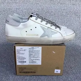 A white leather trainer with a distressed finish standing on a cardboard box