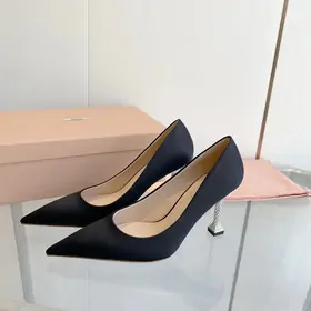 Black satin pointed-toe pumps with a sparkling heel beside a pink box