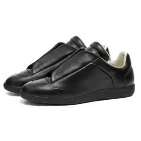 A pair of black leather slip-on trainers with a strap across the top