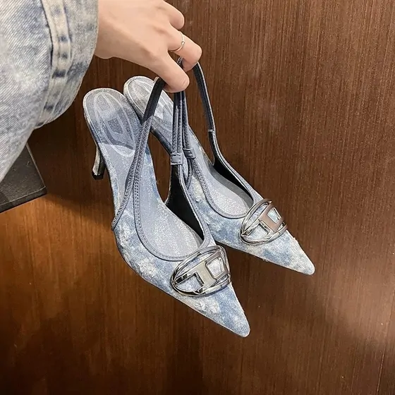 Denim-pattern slingback heels held by hand over a wooden floor