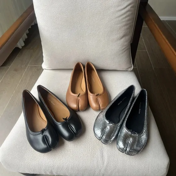 Split-toe ballet flats in black, tan and silver on a chair cushion