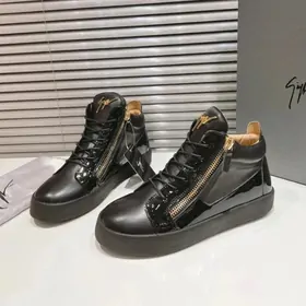A pair of glossy black high-top trainers with side zips on a counter