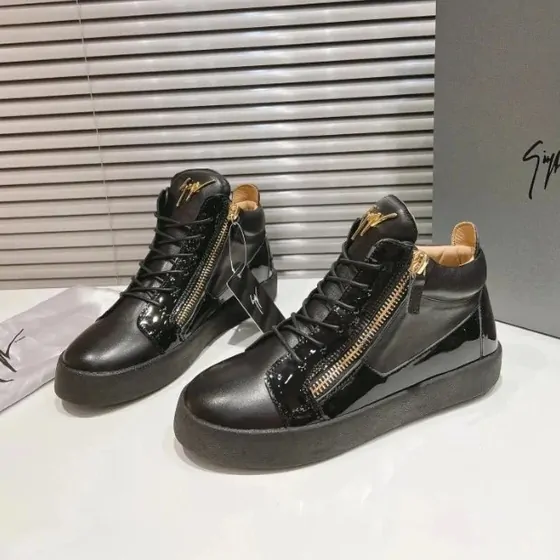 A pair of glossy black high-top trainers with side zips on a counter