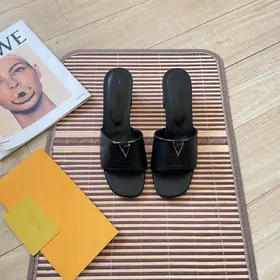 Black leather slide sandals with a metal buckle on a striped mat