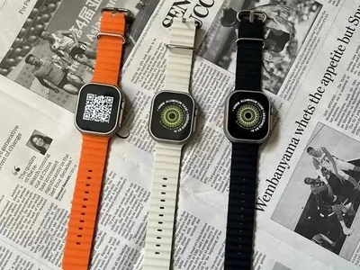 Three smartwatches with orange, white and black straps on newspaper
